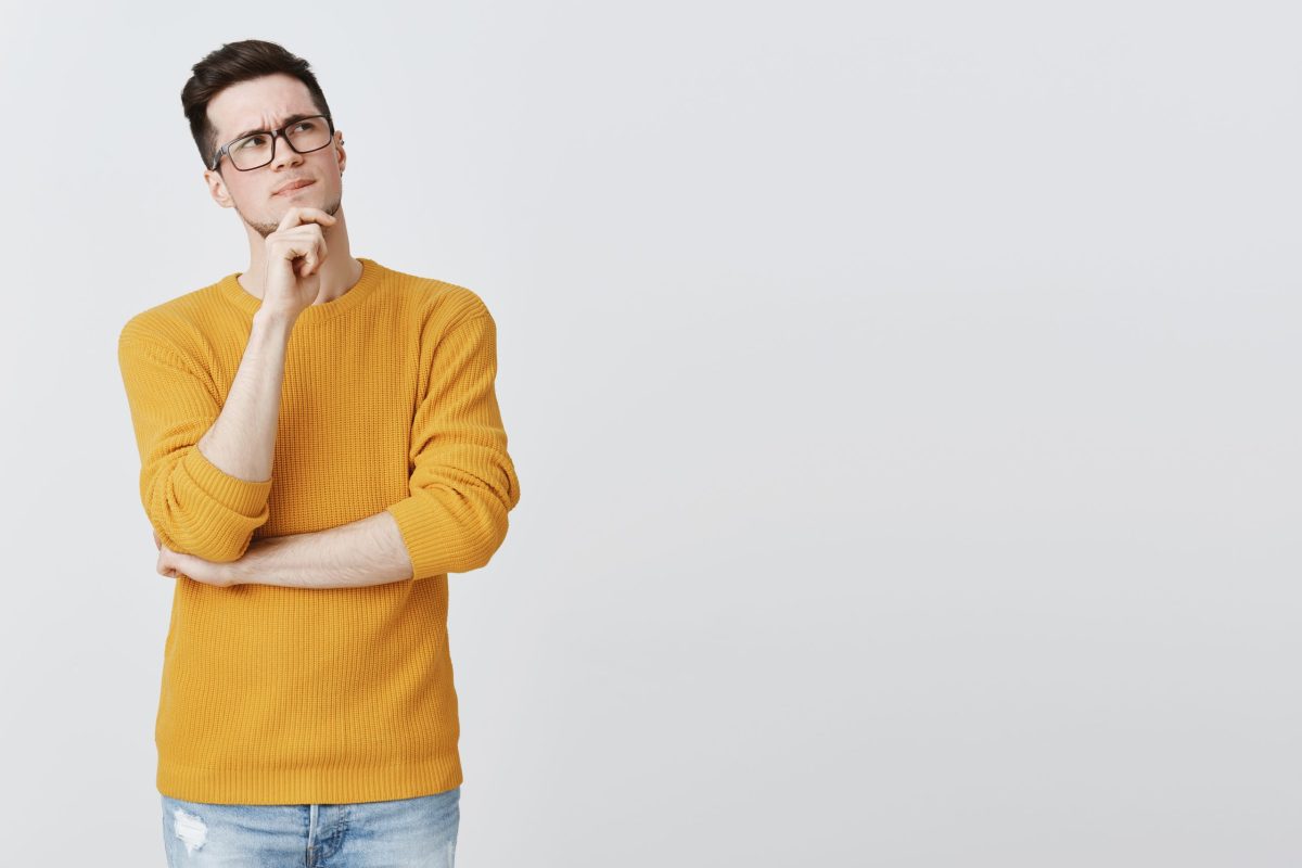 hmm what if. smart and thoughtful good-looking guy in geek glasses and cozy yellow sweater holding hand on chin, frowning and looking at upper right corner as thinking, making decision or assumption